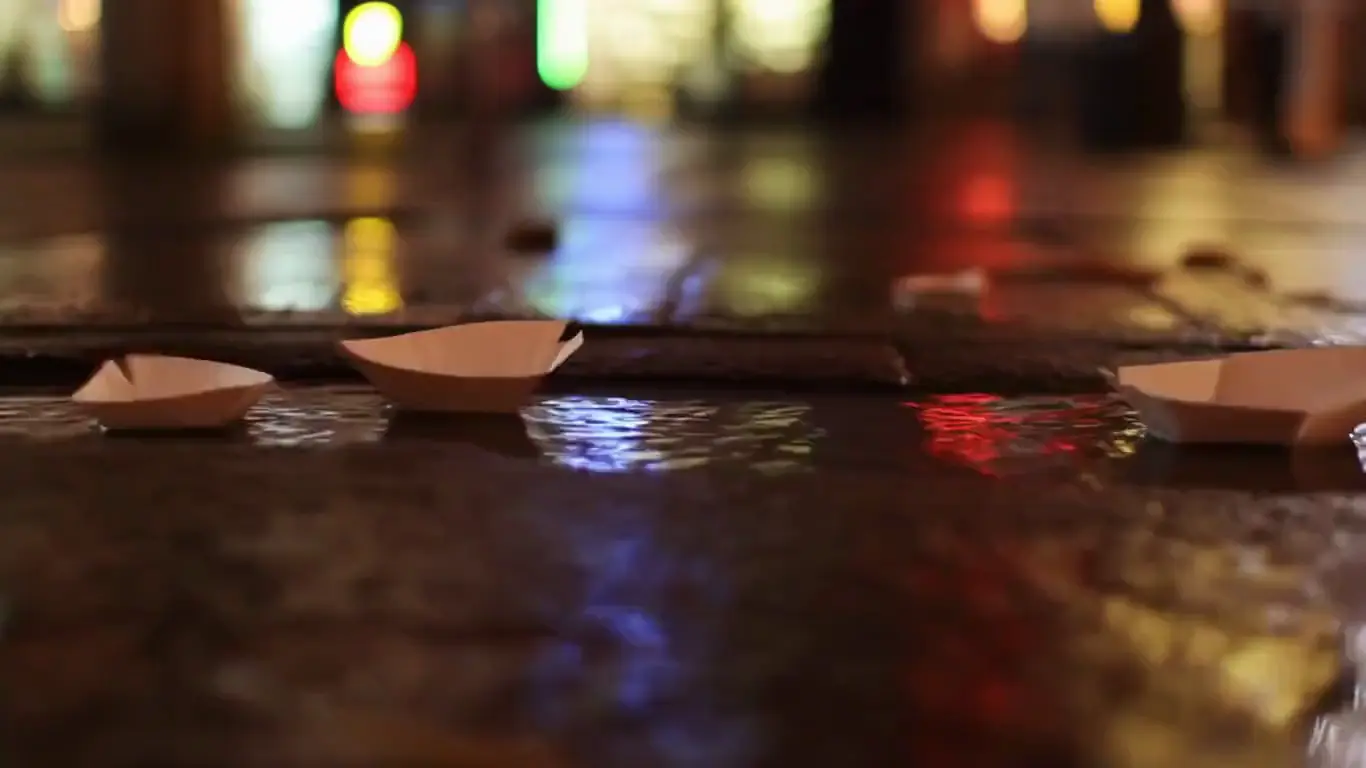 Paper boats drifting down a rain-fed gutter stream past